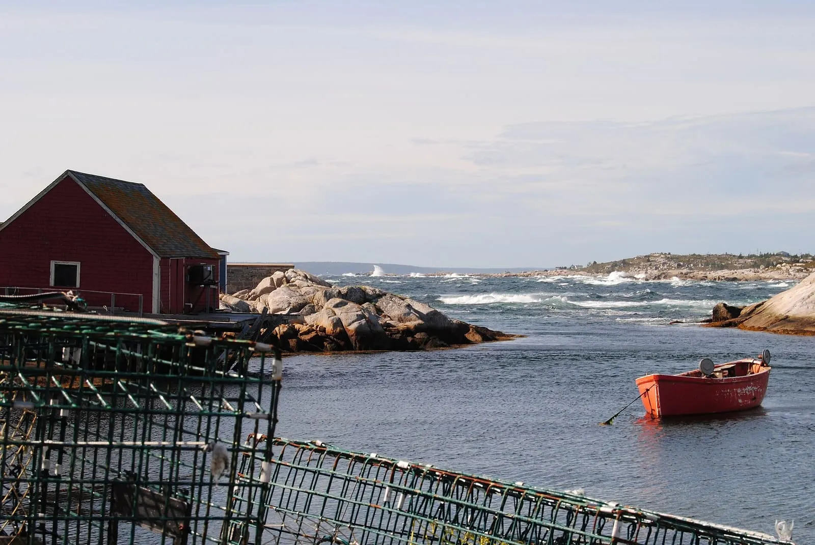 Lobster traps on a wharf at Peggy's Cove, Nova Scotia, with a red fishing shed and a dory in the cove